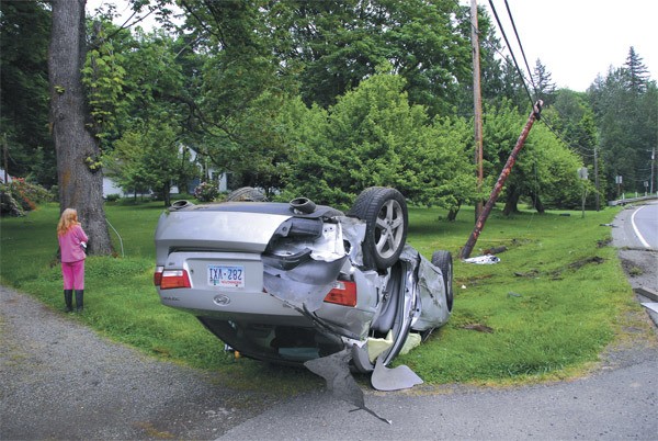 Terri Sahm watches an ongoing accident investigation involving this wrecked car that landed in her front yard the morning of Thursday