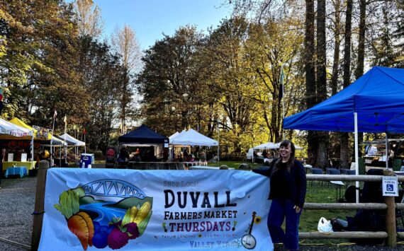 Duvall Farmers Market Board president Alex Yearout stands with the market’s new banner on Oct. 3, 2024. (Grace Gorenflo/Valley Record)