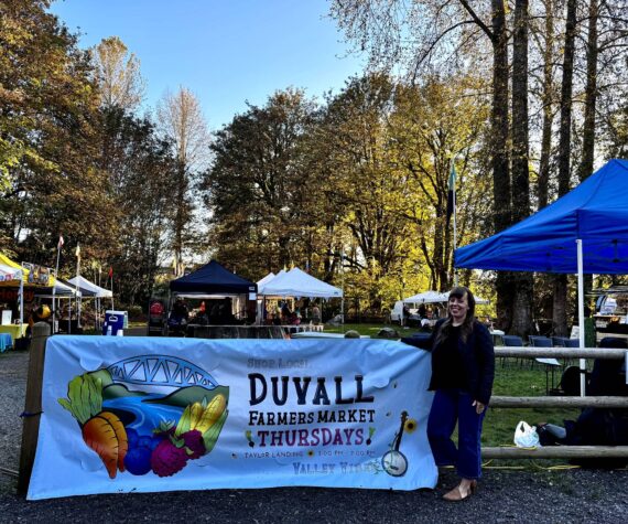 <p>Duvall Farmers Market Board president Alex Yearout stands with the market’s new banner on Oct. 3, 2024. (Grace Gorenflo/Valley Record)</p>